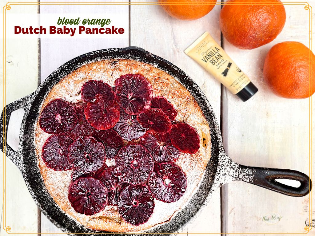 top down view of durch baby pancake in a cast iron skillet topped with blood orange slices and powdered sugar.
