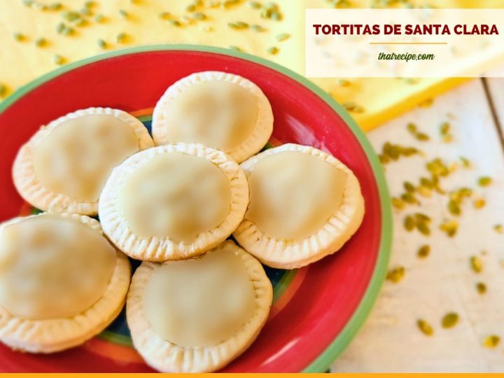 Cookies with a light green glaze on a plate with text overlay Tortitas de Santa Clara