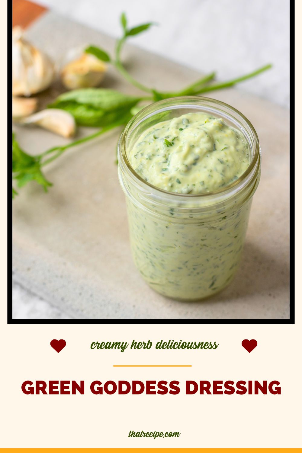 jar filled with green goddess salad dressing on a table with herbs and garlic