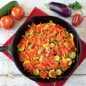 top down view of ratatouille in a skillet with fresh vegetables on a table around it.