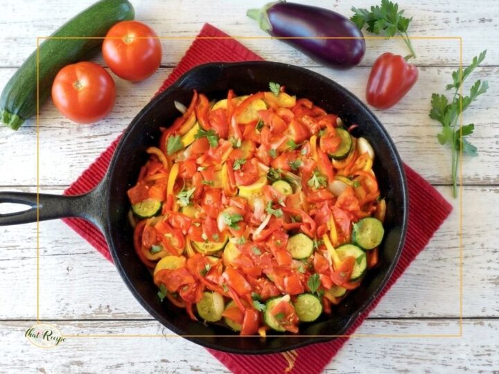 top down view of ratatouille in a skillet with fresh vegetables on a table around it.