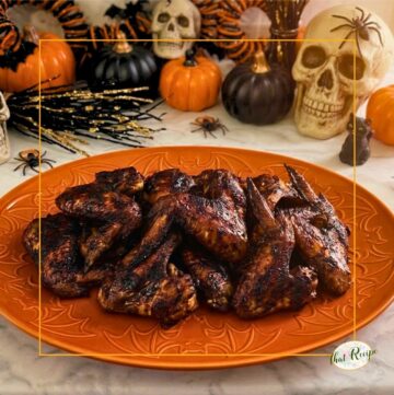chicken wings with a black sauce on a plate with Halloween decor